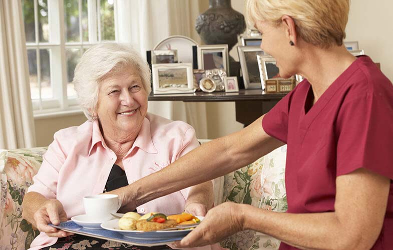 in home care staff assisting a senior with a meal.