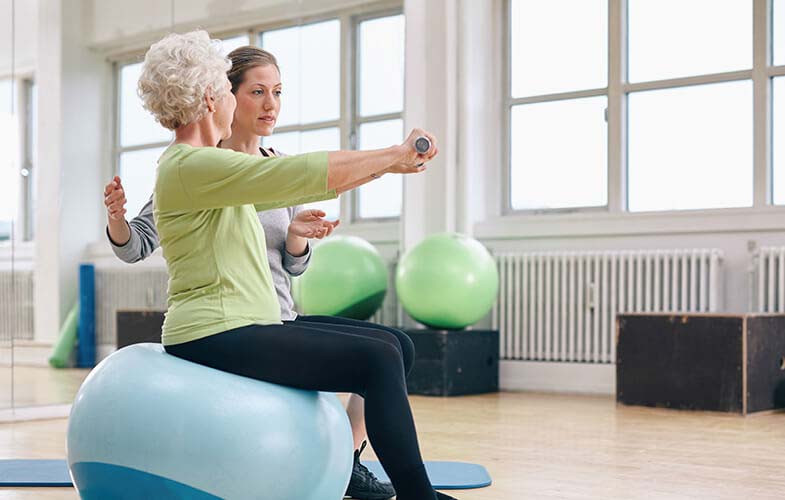 Elderly woman doing rehab therapy with staff.